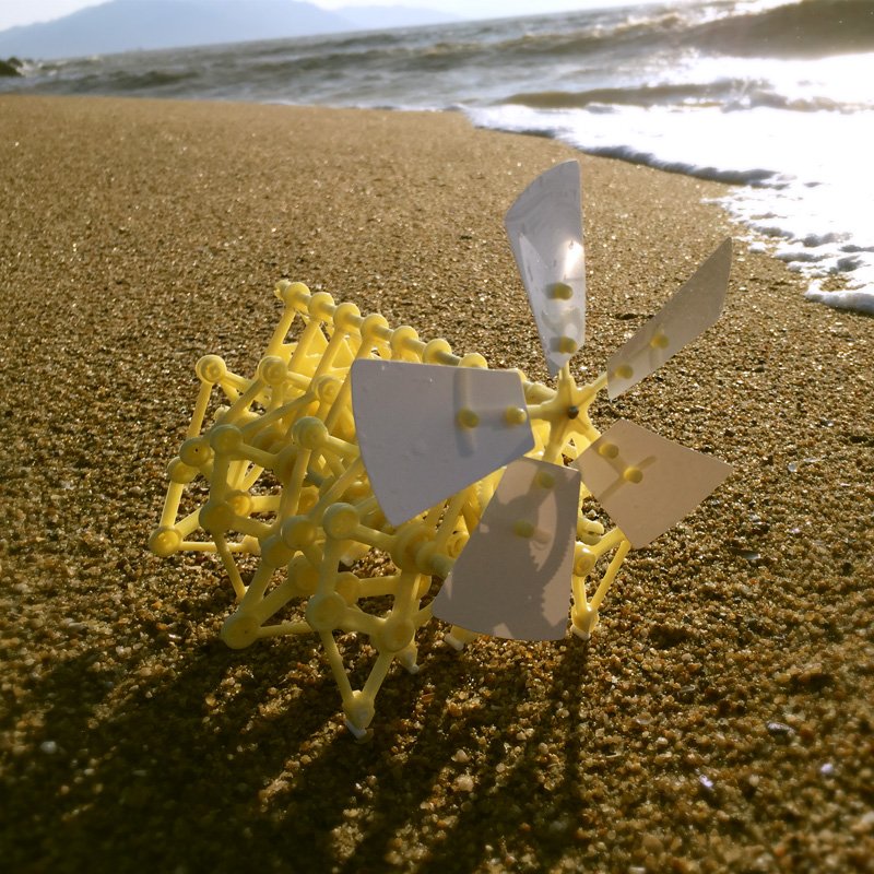 Yellow and gray geometric sculpture on a sandy beach with ocean waves in the background