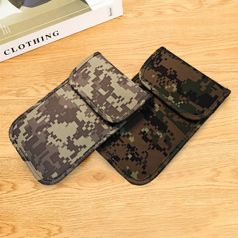 Two camouflage phone pouches with digital pixel patterns in green, brown, and gray, displayed on a light wood surface next to a book.