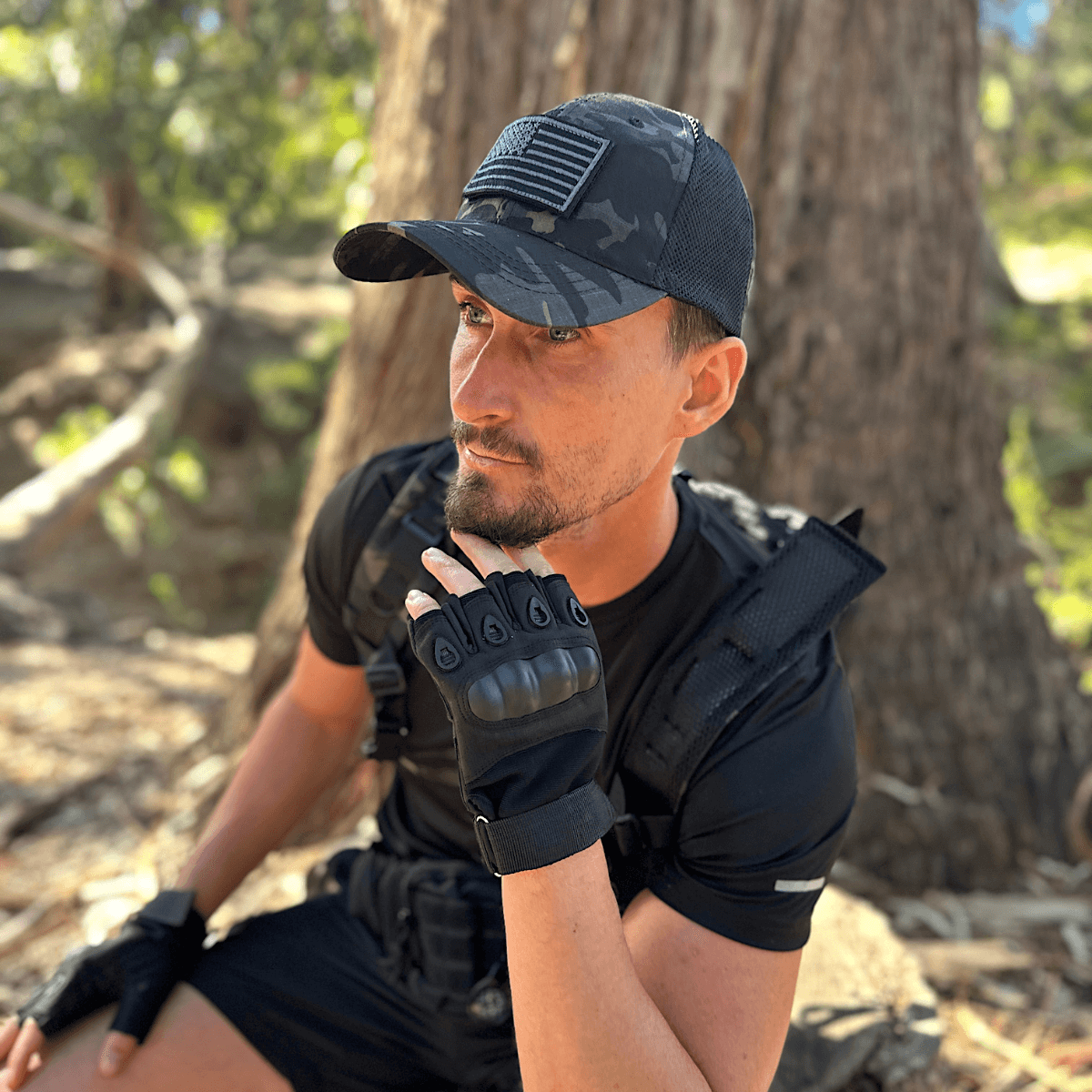 Man in tactical gear sitting outdoors with trees in the background