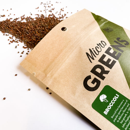Kraft paper package labeled 'Micro Greens Broccoli' with scattered seeds on a white background